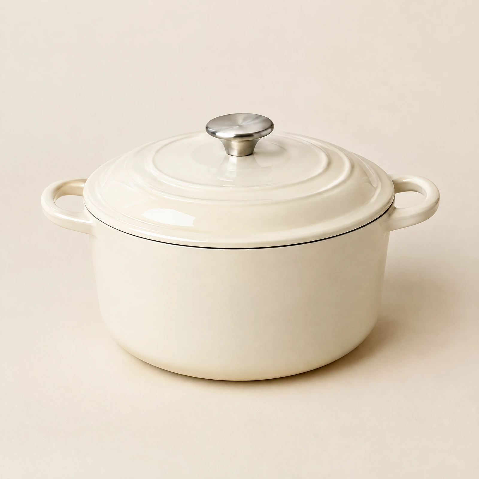 Round glossy cream Dutch oven with lid, silver-tone knob and two loop handles on a cream backdrop