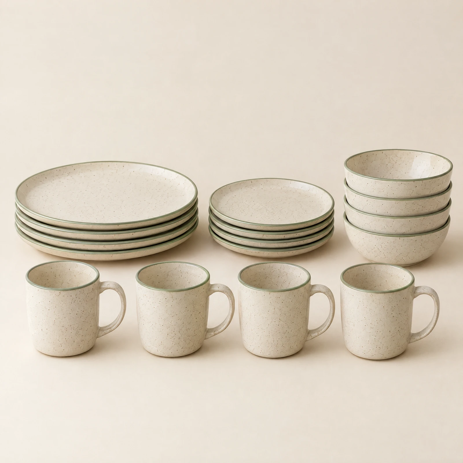 Sixteen piece speckled cream dinnerware set with sage rims: stacked plates, bowls and mugs on a cream backdrop