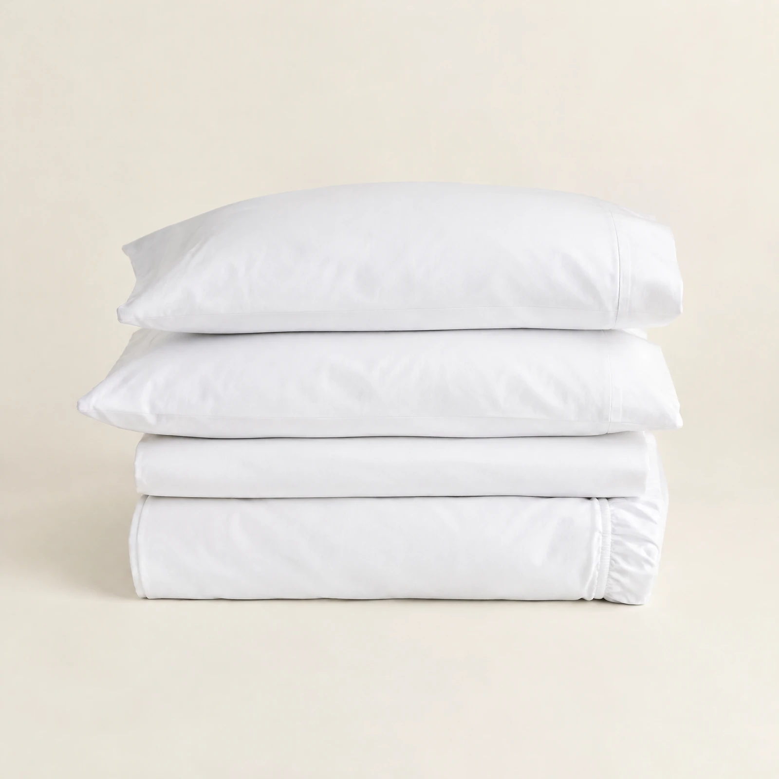 Four-piece white sheet set folded in a neat stack with two pillowcases on top against a cream backdrop